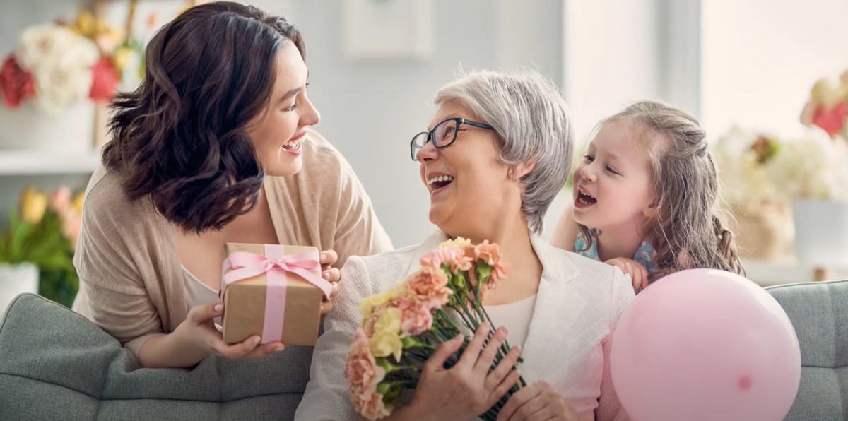 a mom holding a bouquet while receiving a gift from her daughter and granddaughter