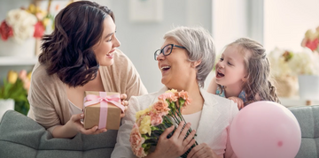 a mom holding a bouquet while receiving a gift from her daughter and granddaughter